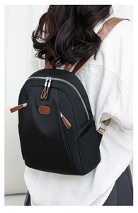 Rear view of a black nylon backpack with brown straps and zippers shown on a model