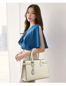 Close-up of beige croc-embossed tote bag with silver charm held by a model