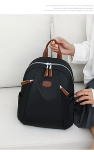 Close-up of black nylon backpack with brown leather details on a white sofa