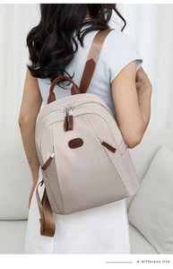 Detail of beige nylon backpack with brown leather trim and silver zipper on a model