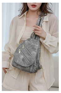Detalle de bolso de pecho gris en cuero lavado con cremalleras doradas y textura vintage suave