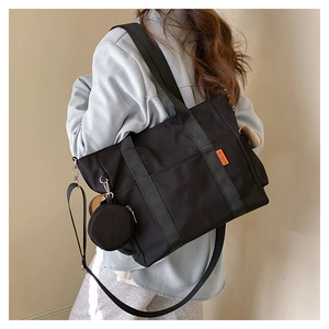 Detail of a black canvas tote bag showing the side logo, handle, and a mini round coin purse