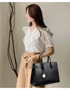 Detail shot of a black geometric paneled tote bag held by a model for a chic commute look