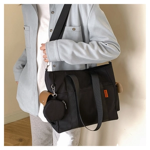 Detail of black nylon tote bag featuring orange label and small round coin purse attachment