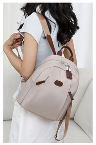 Side view of a beige nylon backpack for women with brown leather trim and zipper details
