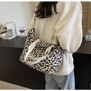 Leopard print tote bag with white handles and adjustable strap shown on model in cafe