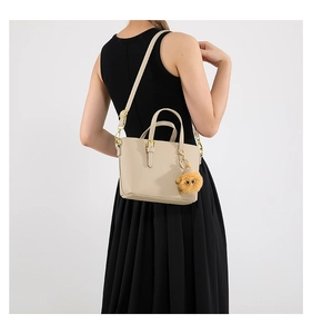 Detail of beige textured bucket bag featuring gold hardware and a cute brown plush charm