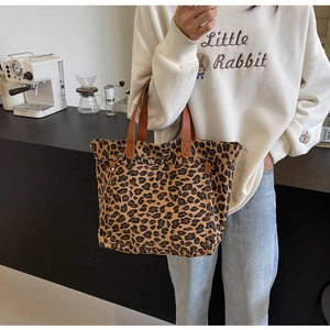 Close-up of leopard print canvas tote bag featuring brown leather handles and rivet detail