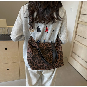 Detail of leopard print canvas tote bag featuring black handles and wide shoulder strap