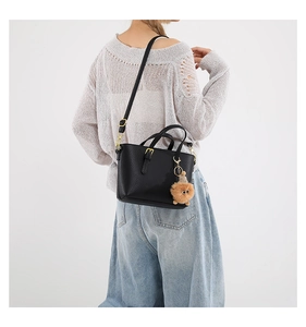 Detail view of black lychee grain leather bucket bag with cute brown plush charm on a model