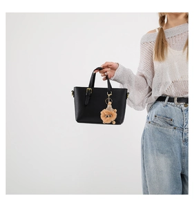 Close-up of black litchi leather bucket bag featuring a cute lion plush pendant detail