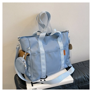 Macro view of light blue nylon tote bag showing brown leather pocket and small round pouch