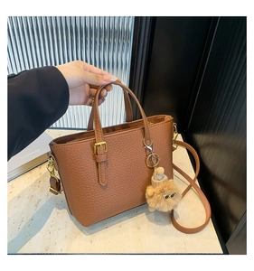 Detail of a brown lychee pattern leather bucket bag with a cute plush bear charm