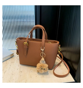 Close-up of brown textured leather bucket bag with gold hardware and plush monster charm