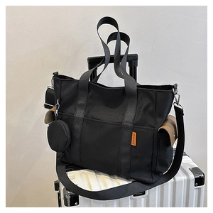 Large black canvas tote bag on white suitcase with orange label and mini round coin purse