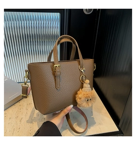 Close-up of brown textured bucket bag with dual handles and animal plush charm