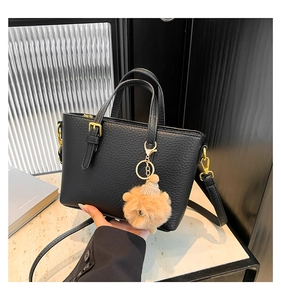 Detail view of black litchi texture handbag featuring golden hardware and plush bear charm