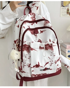 Détail du sac à dos blanc avec imprimé paysage rouge, charme peluche et logo JXING