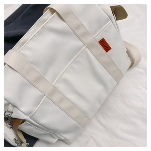 Detail of cream tote bag with orange brand tag, wide strap and silver zipper closure