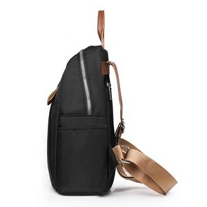 Minimalist black nylon backpack with brown leather trim shown from a side angle