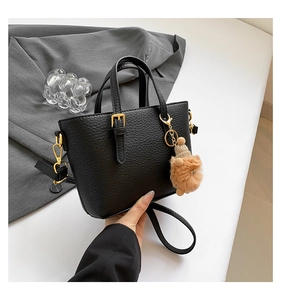 Detail of black lychee leather bucket bag with gold hardware and plush charm pendant