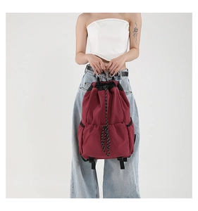 Front view of burgundy nylon drawstring backpack on model with side pockets and buckles