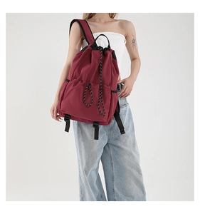 Side view of a burgundy drawstring nylon backpack featuring decorative black and white ropes