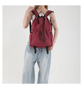 Detail of burgundy waterproof nylon drawstring backpack with striped cord on woman's back