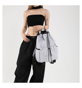 Close-up of a light grey nylon drawstring backpack with black cords and side pocket
