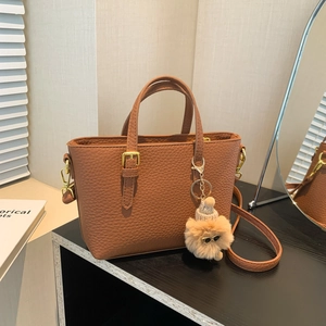 Brown litchi grain bucket bag with dual handles and plush charm on black pedestal