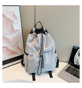 Detail view of light grey drawstring backpack featuring black woven cords and side pockets