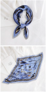 Detail of pleated blue silk scarf featuring equestrian motifs and chain patterns