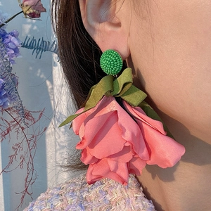 Pink fabric floral drop earrings with green bow accent on model for resort fashion