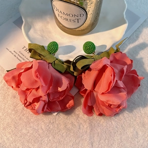 Macro detail of large pink fabric flower earrings with green ribbon bows on soft white fur