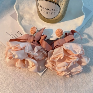 Detail of handmade light pink fabric flower earrings with satin bows on white fur