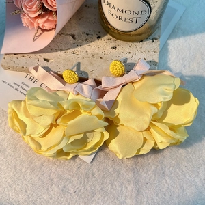 Macro detail of large yellow fabric floral earrings with soft pink ribbon bows