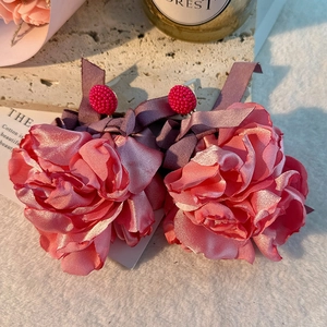 Detail of pink silk flower earrings with purple ribbon bow on a textured background