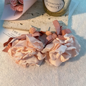 Detail of pink fabric flower earrings with ribbon bows on a marble and plush surface