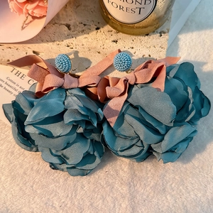 Detail of blue fabric flower earrings with pink suede bows and beaded studs on stone