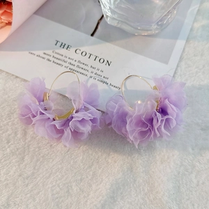 Details von hellvioletten Chiffon-Blumenohrringen mit Goldringen auf weißem Kunstpelz
