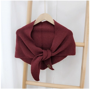 Detail of burgundy knitted shawl with textured stitching and small leather brand label