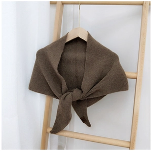 Detail of dark brown knitted shawl draped on wooden ladder with a subtle fabric label