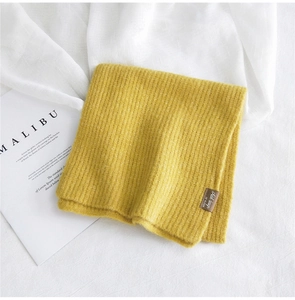 Dettaglio della sciarpa in maglia a coste giallo zenzero con etichetta in pelle e lana
