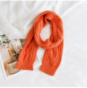 Detailed view of bright orange cable knit scarf with thick wool texture and ribbed edges