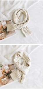 Detailed knit texture of a thick cream cable-knit scarf on minimalist white background