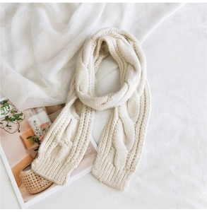 Detail of cream cable-knit scarf showing thick soft texture and intricate woven patterns