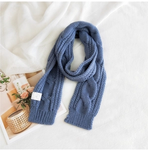 Close-up of fog blue cable-knit scarf with ribbed edges and white decorative label