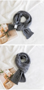 Detailed texture of thick dark grey cable knit scarf with a minimalist white fabric label