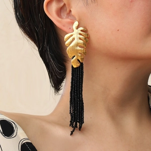 Detail of long gold leaf earrings with hanging black seed bead tassels on a female model