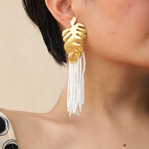 Close-up of golden monstera leaf earrings with long white beaded tassels on model